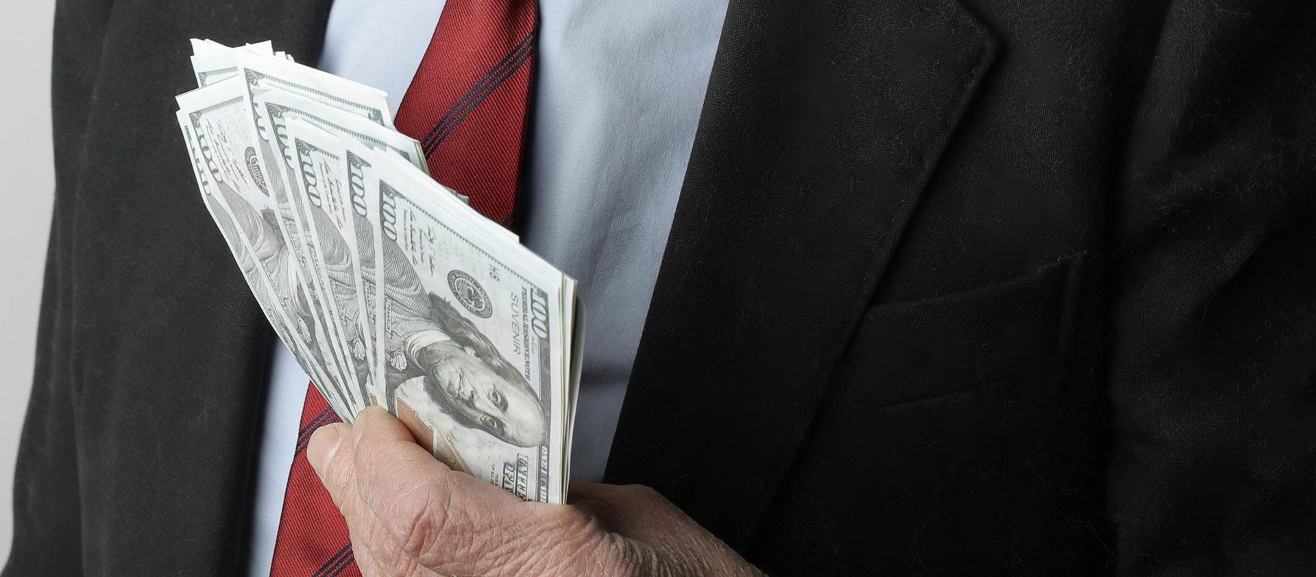 A man in a suit holds a large amount of US dollars in his hand